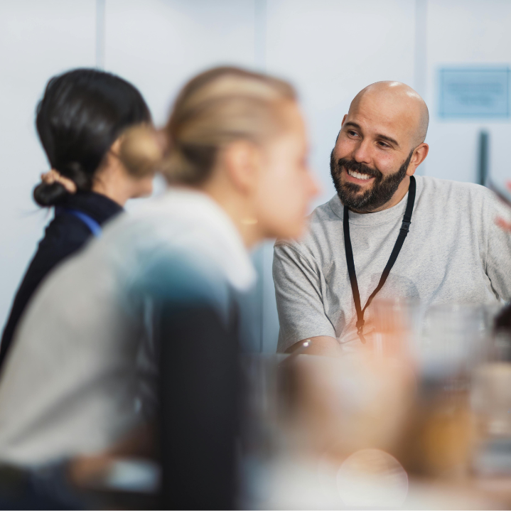 Man with a beard and lanyard smiling among people in an office setting