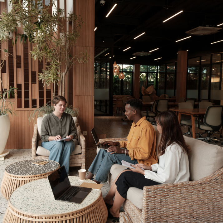 Three people sitting in a modern office lounge area with a laptop on a table.