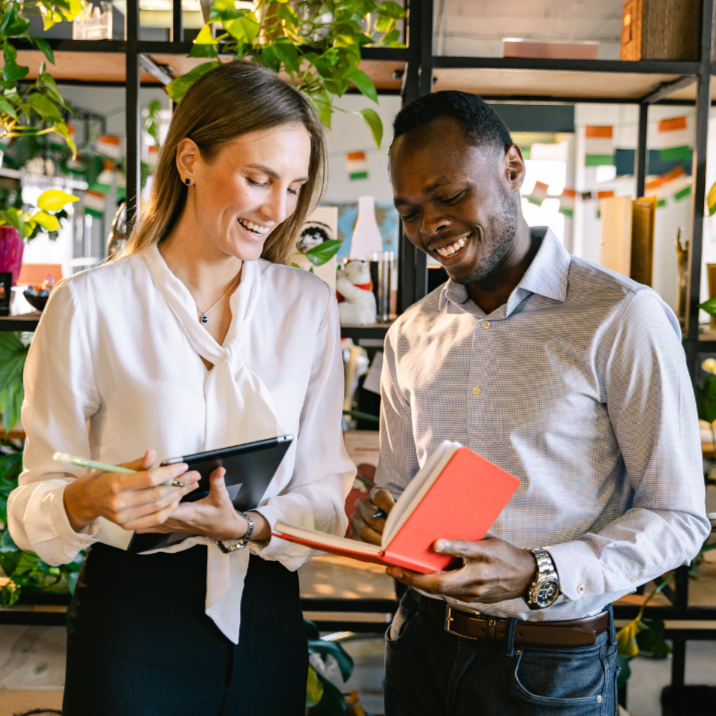 Two people in a modern office setting with plants and shelves.