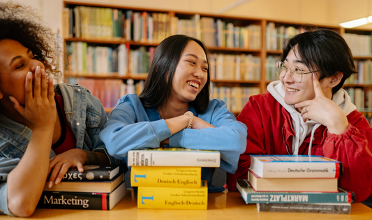 Diverse group of young professionals smiling and studying together in a library with career and marketing books, symbolizing career growth and professional success.