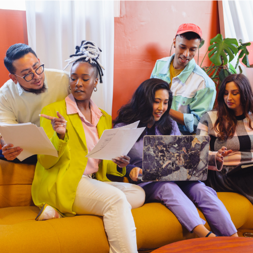 Five people sitting on a couch, engaged with various devices in a casual setting.