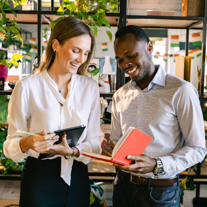 Two people in a modern office setting with plants and shelves.